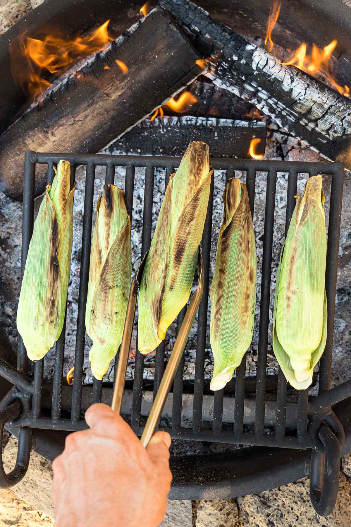 A hand turning corn on the grill using metal tongs