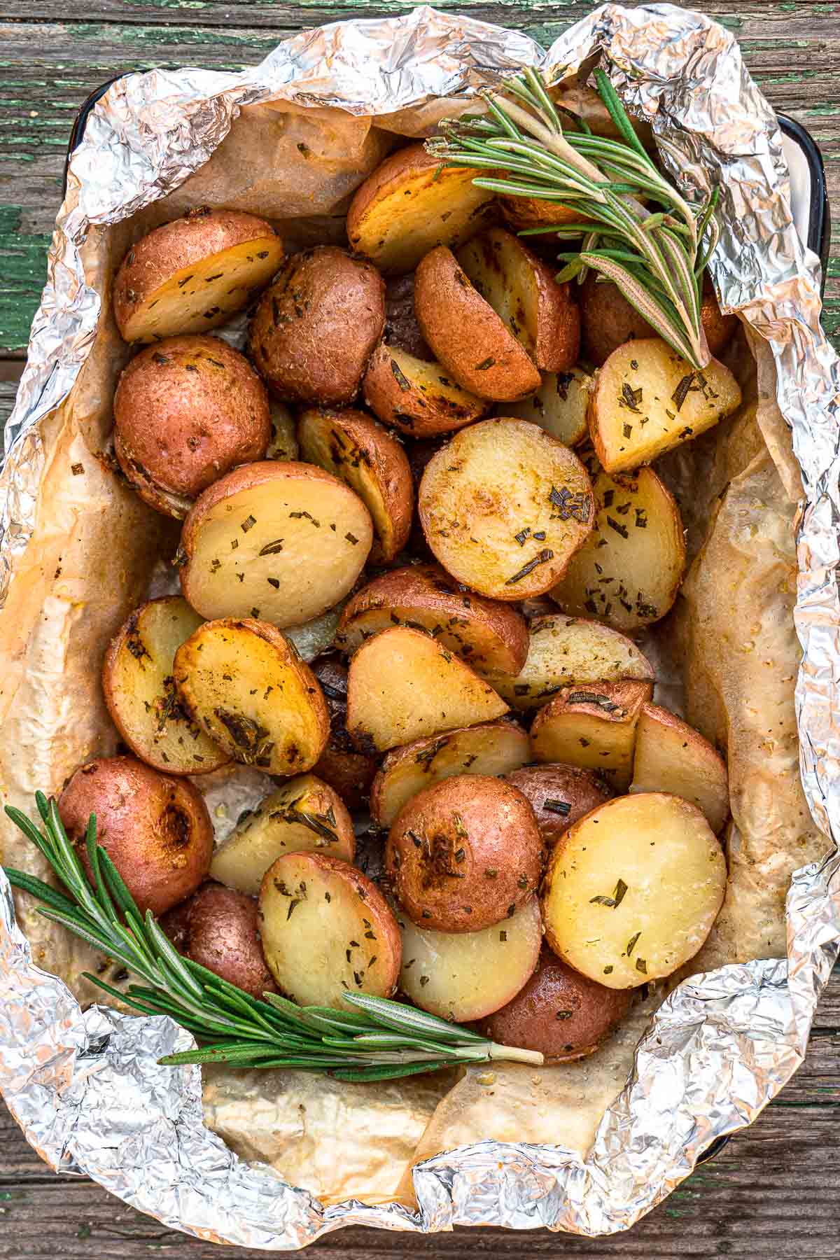 Grilled potatoes in foil garnished with rosemary sprigs