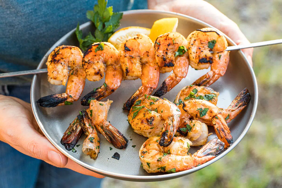 Hands holding a plate of grilled shrimp