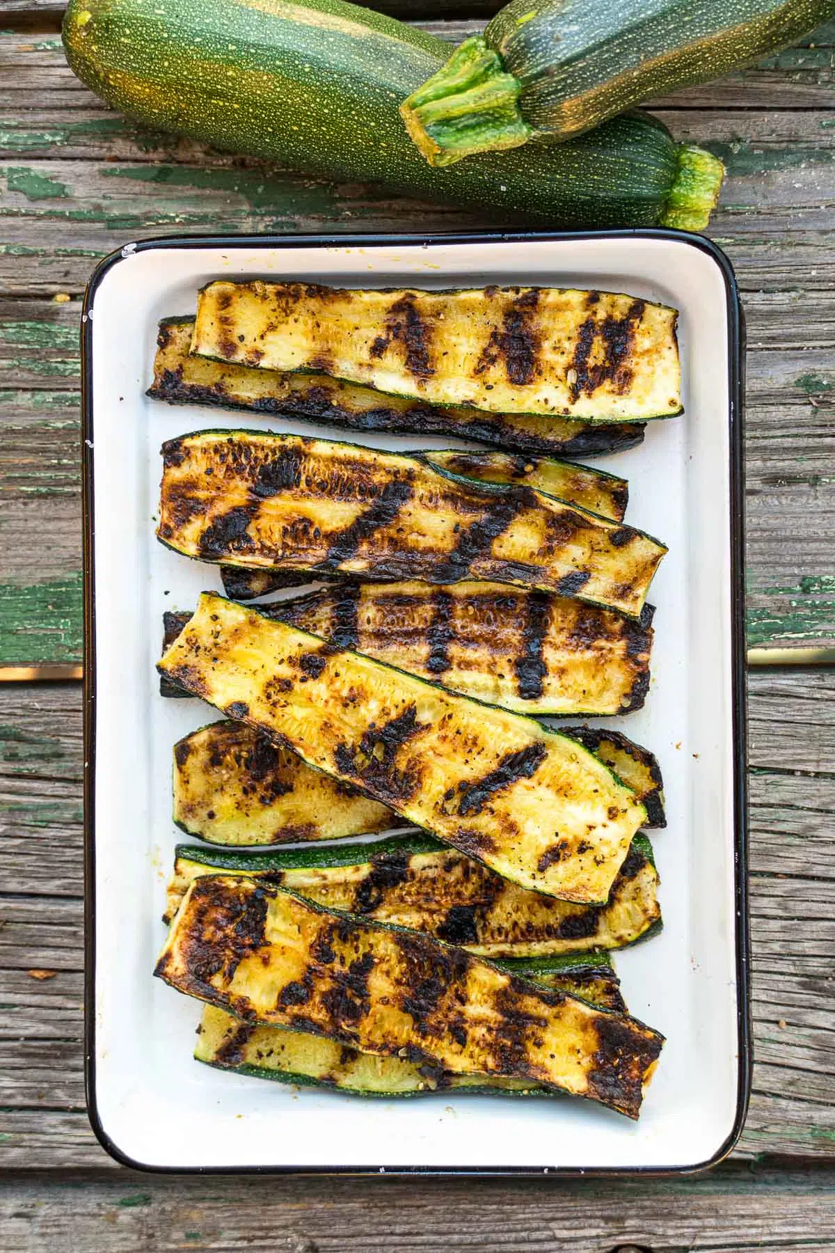 Grilled zucchini in a white enamel dish with fresh zucchinis in frame