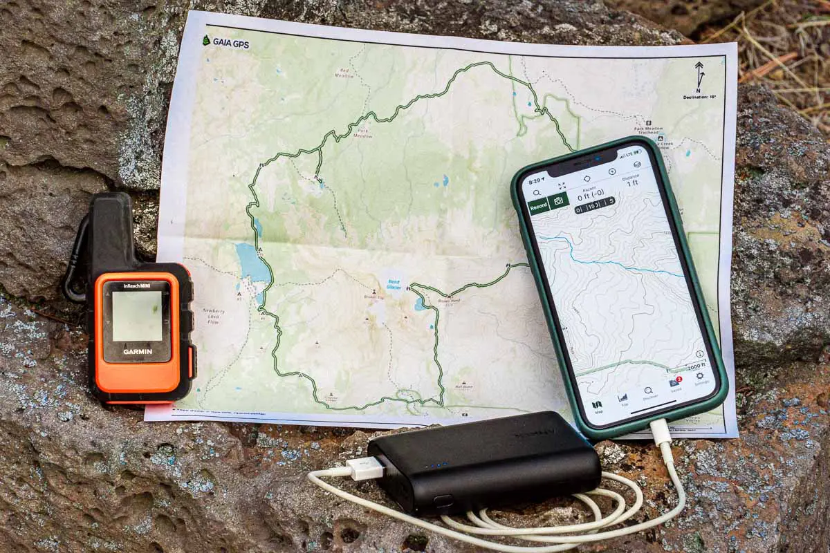 A paper map, satellite messenger, and phone with GPS
