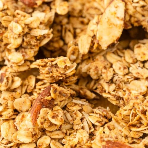 Close-up of granola clusters with oats, sliced almonds, and nuts, showing a golden brown color and toasted texture.