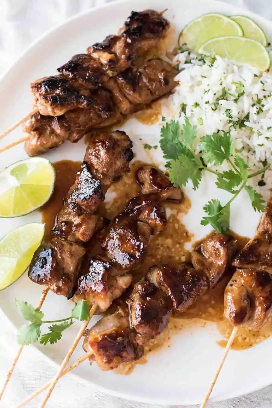 Three juicy grilled chicken skewers served with cilantro-lime rice and lime wedges on a white plate, ready to delight the taste buds.