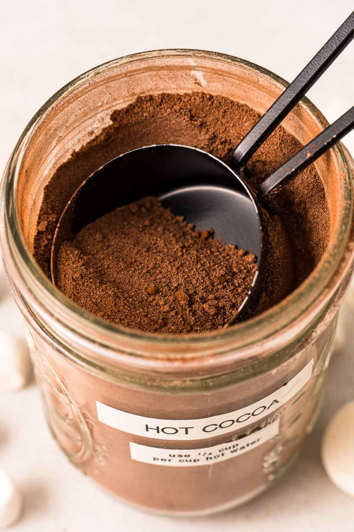 A top view of a mason jar full of hot cocoa mix with a ¼ cup measure scooping the mix out for homemade hot cocoa.