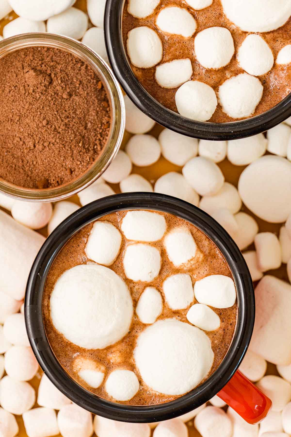 A close-up of two mugs of marshmallow-topped hot cocoa. 
