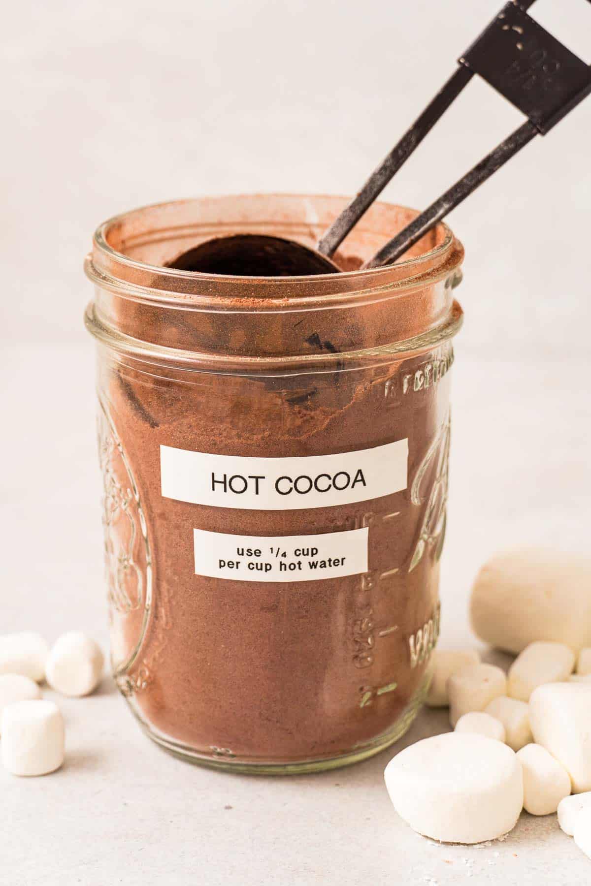 A mason jar with hot cocoa and a ¼ cup scoop inside. The label reads “hot cocoa, use ¼ cup hot cocoa per cup hot water.”