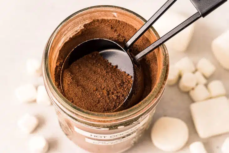 A top view of a mason jar full of hot cocoa mix with a ¼ cup measure scooping the mix out for homemade hot cocoa.