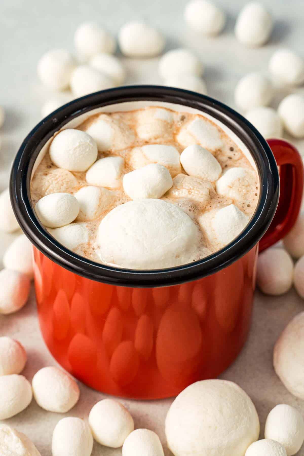 A red mug full of hot cocoa made with DIY hot cocoa mix and topped with crunchy dehydrated marshmallows.