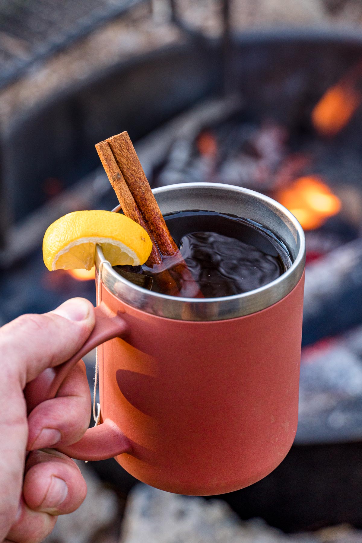Hand holding a mug of hot toddy with a cinnamon stick and lemon slice