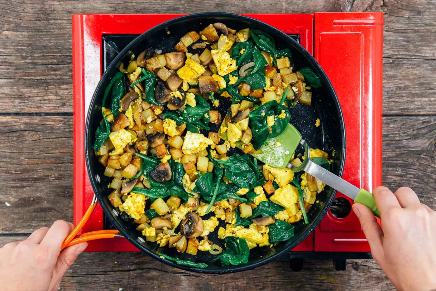 Cooking scrambled tofu with spinach in a large skillet on a camping stove