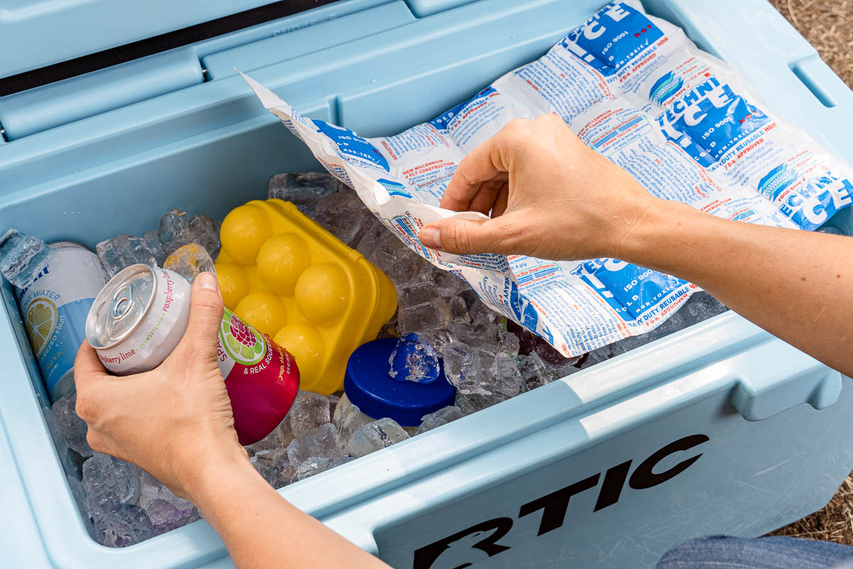 Hands reaching into a blue cooler full of ice to pick up a drink can