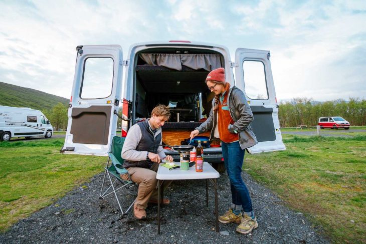 A couple cooking in front of a camper van