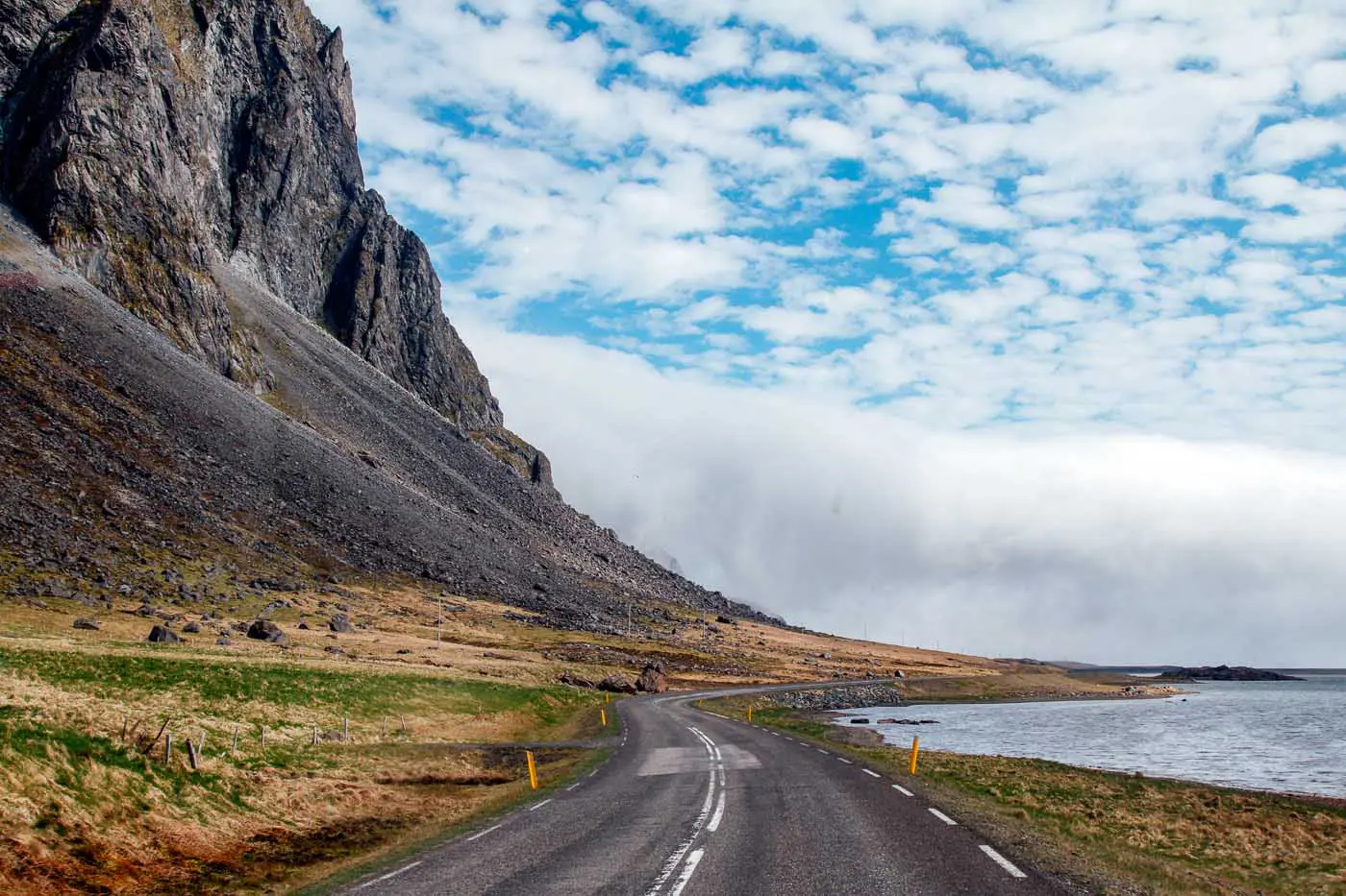 An empty road in Iceland. There are black mountains on the left and the ocean on the right.