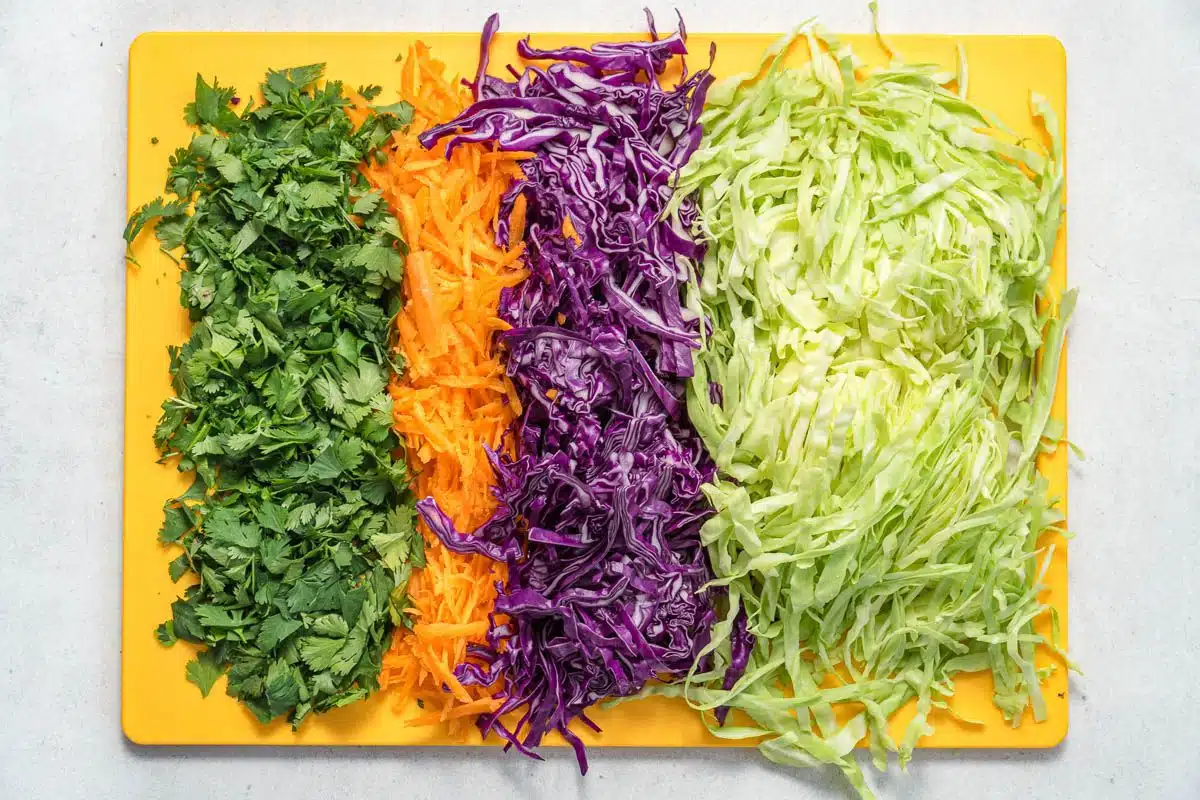 Shredded cabbage, carrots, and cilantro on a cutting board.