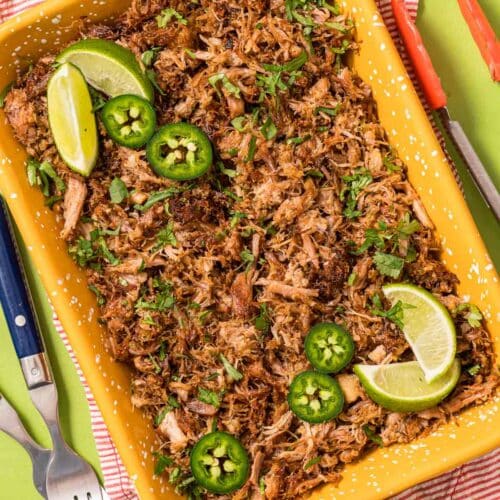 Instant Pot Carnitas served on an orange dish with fresh limes and slices of jalapeno peppers.