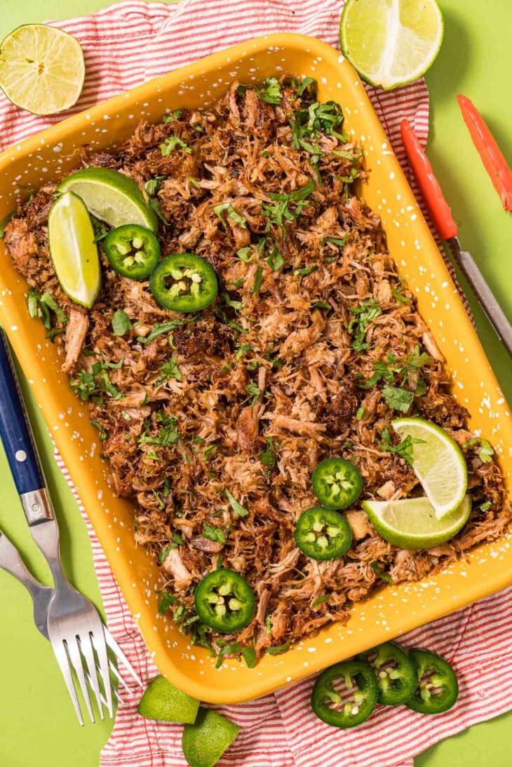 Instant Pot Carnitas served on an orange dish with fresh limes and slices of jalapeno peppers.