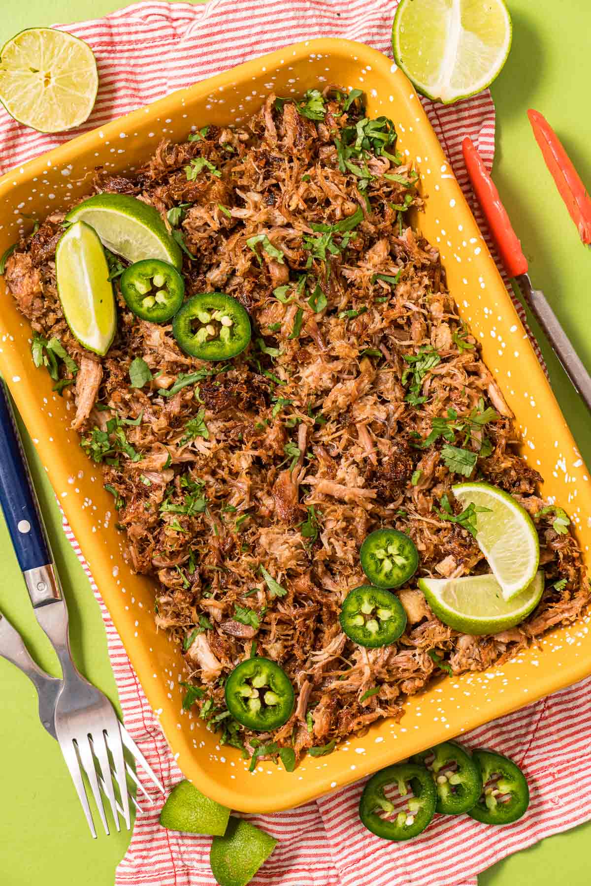 Instant Pot Carnitas served on an orange dish with fresh limes and slices of jalapeno peppers. 