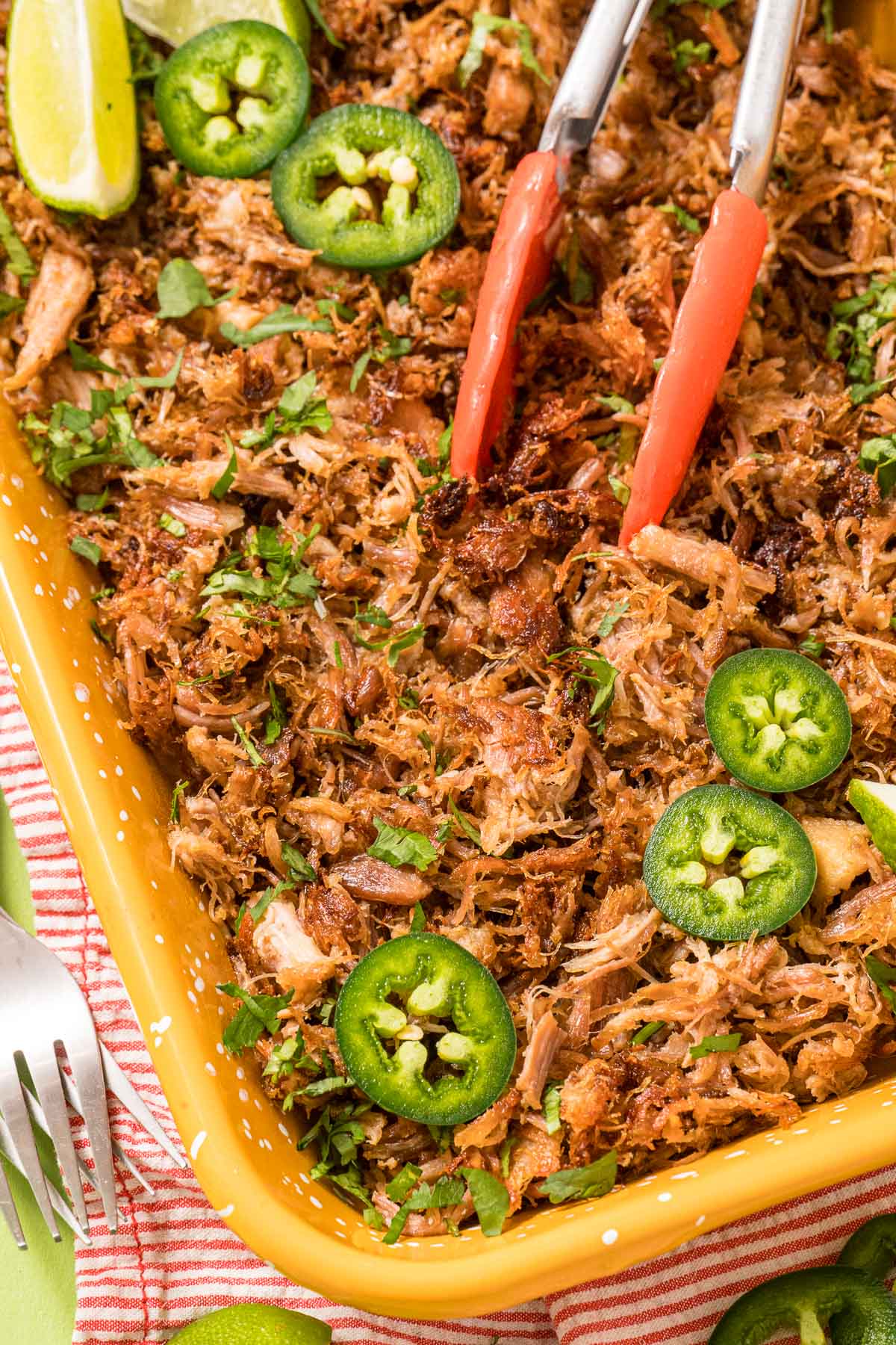 Instant Pot Pork Carnitas served in a dish with fresh limes and slices of jalapeno peppers.