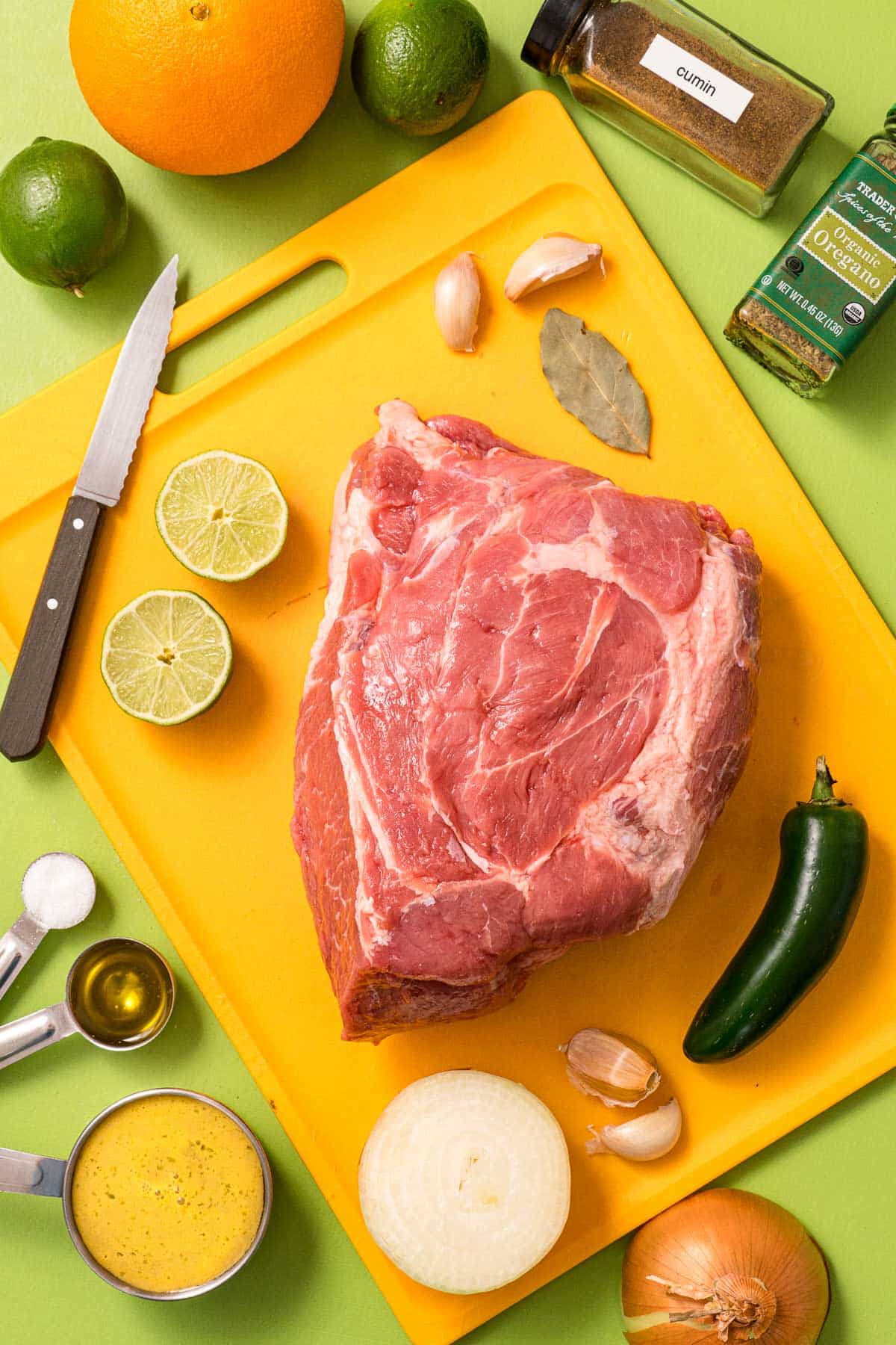 A pork shoulder and the ingredients for Instant Pot carnitas on a cutting board. 