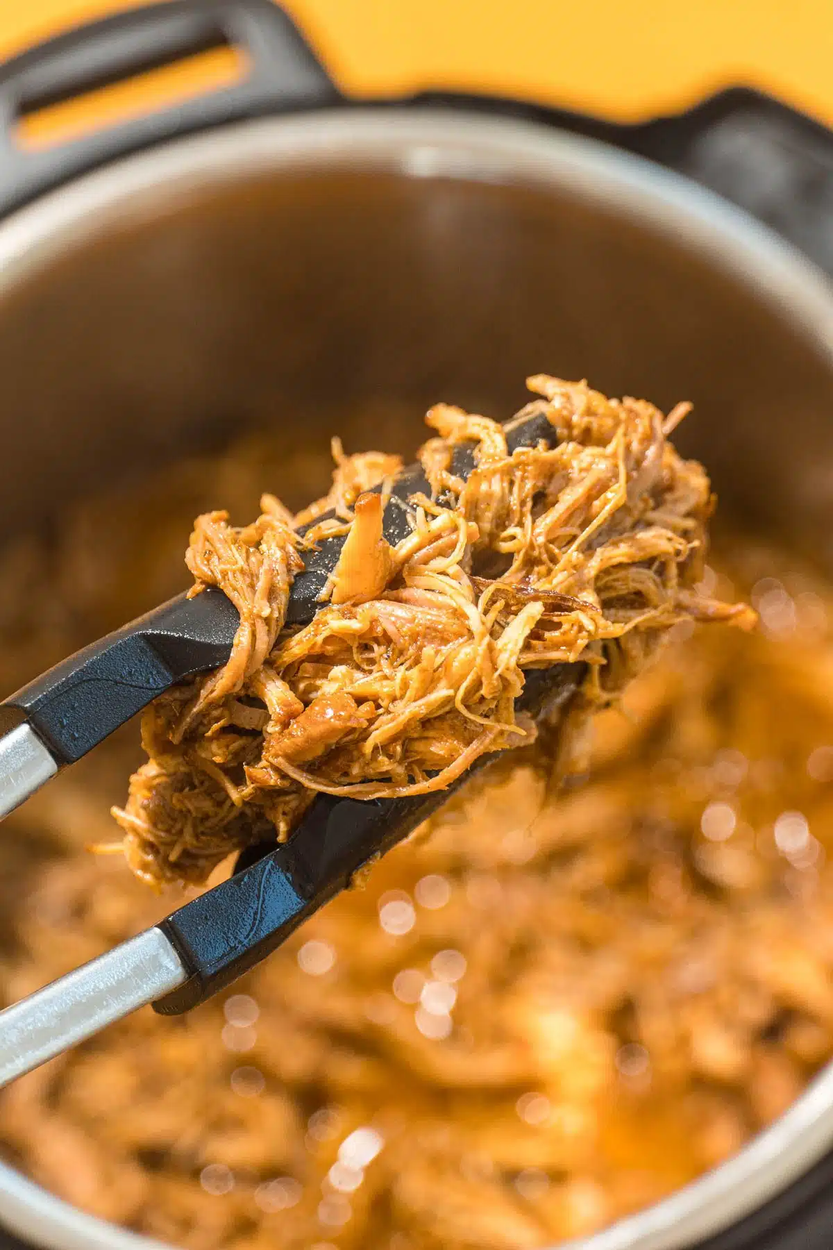 A pair of tongs lifting BBQ pulled pork out of an Instant Pot.