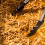 BBQ pulled pork in an Instant Pot with a pair of tongs.