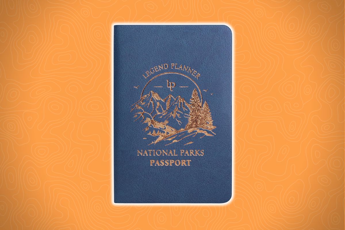 A blue notebook with gold mountain and tree illustrations on the cover sits on an orange background with a faint topographic map pattern.