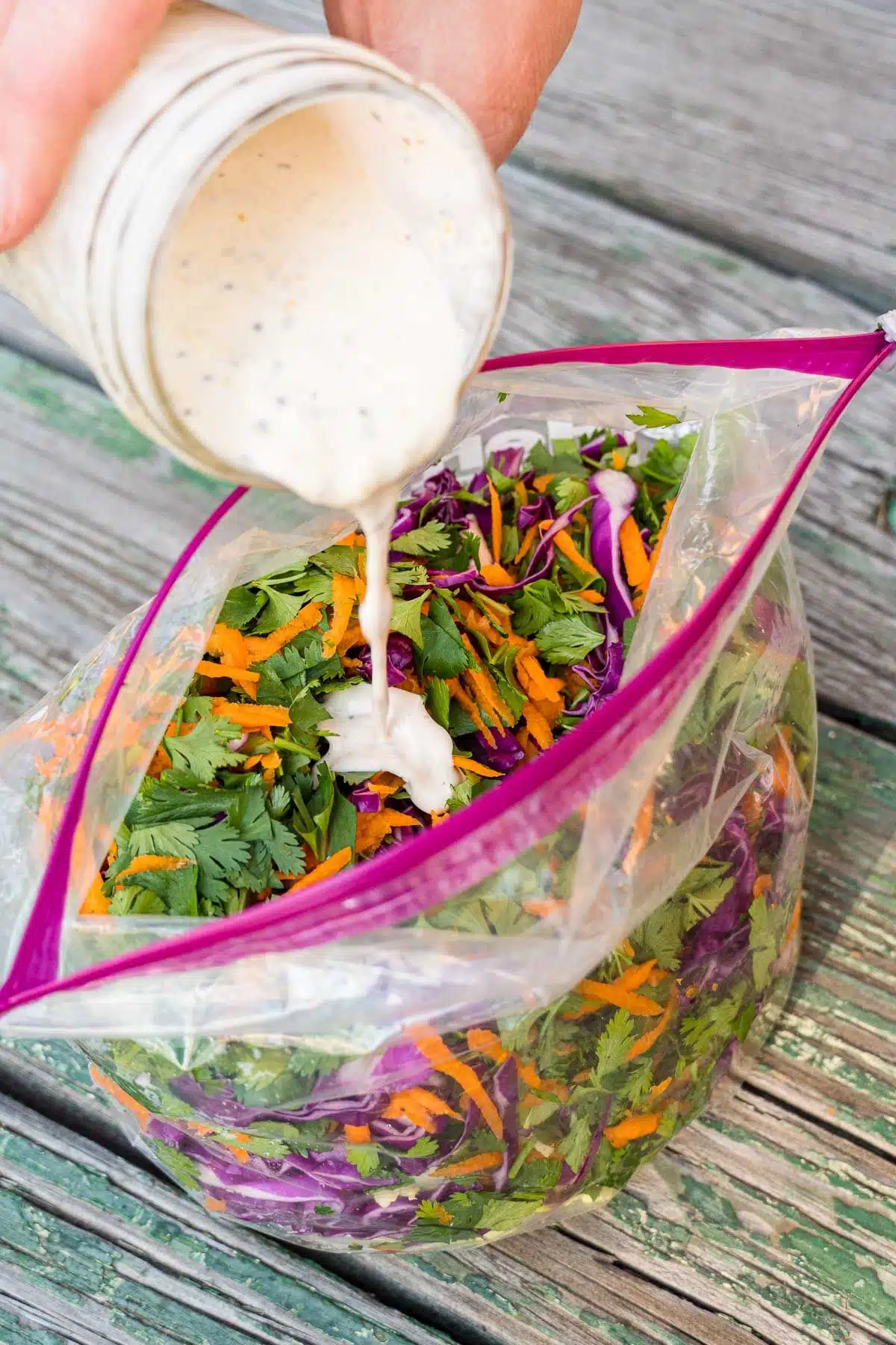 Pouring dressing into a bag with cabbage, carrots, and cilantro.