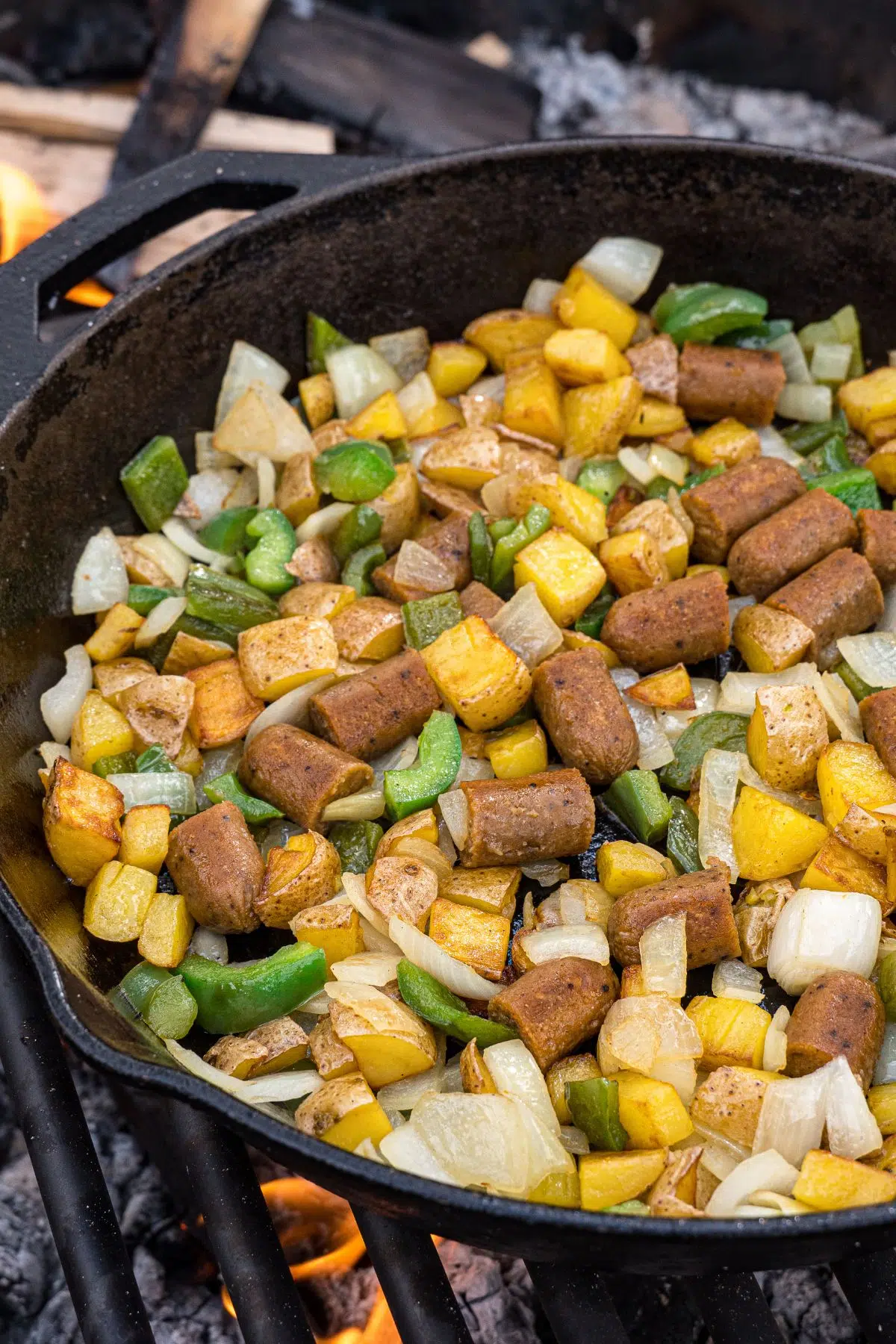 Sausage, peppers, onions, and potatoes cooking in a cast iron skillet