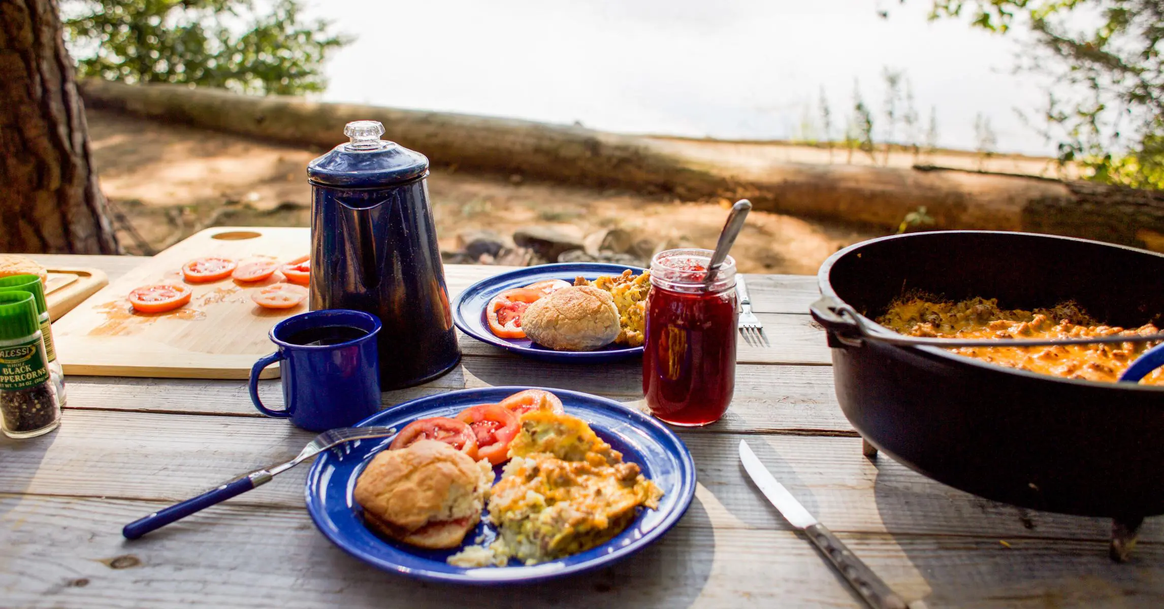 A camp scene with a pot of coffee, blue plate with egg breakfast, and Dutch oven in frame