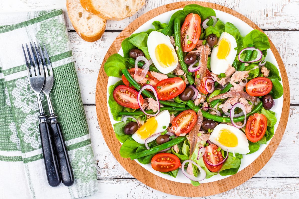 Nicoise salad with sliced eggs, tuna, tomatoes, and greens on a plate.