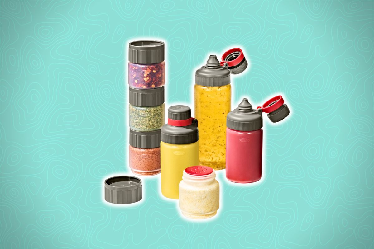 A set of clear stackable containers with gray lids, filled with various colorful contents, on a light teal background with wavy pattern.