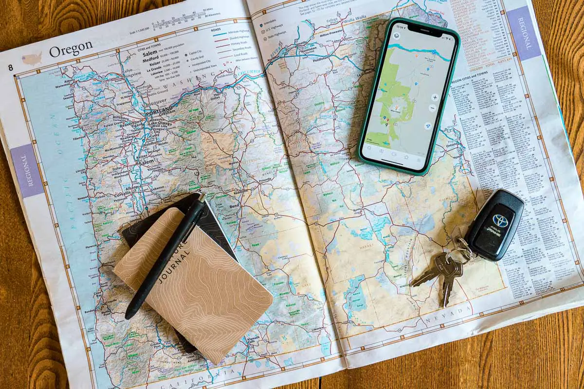 An atlas opened to show a map of Oregon. A notebook and pen, car keys, and a cell phone rest on top of the map.