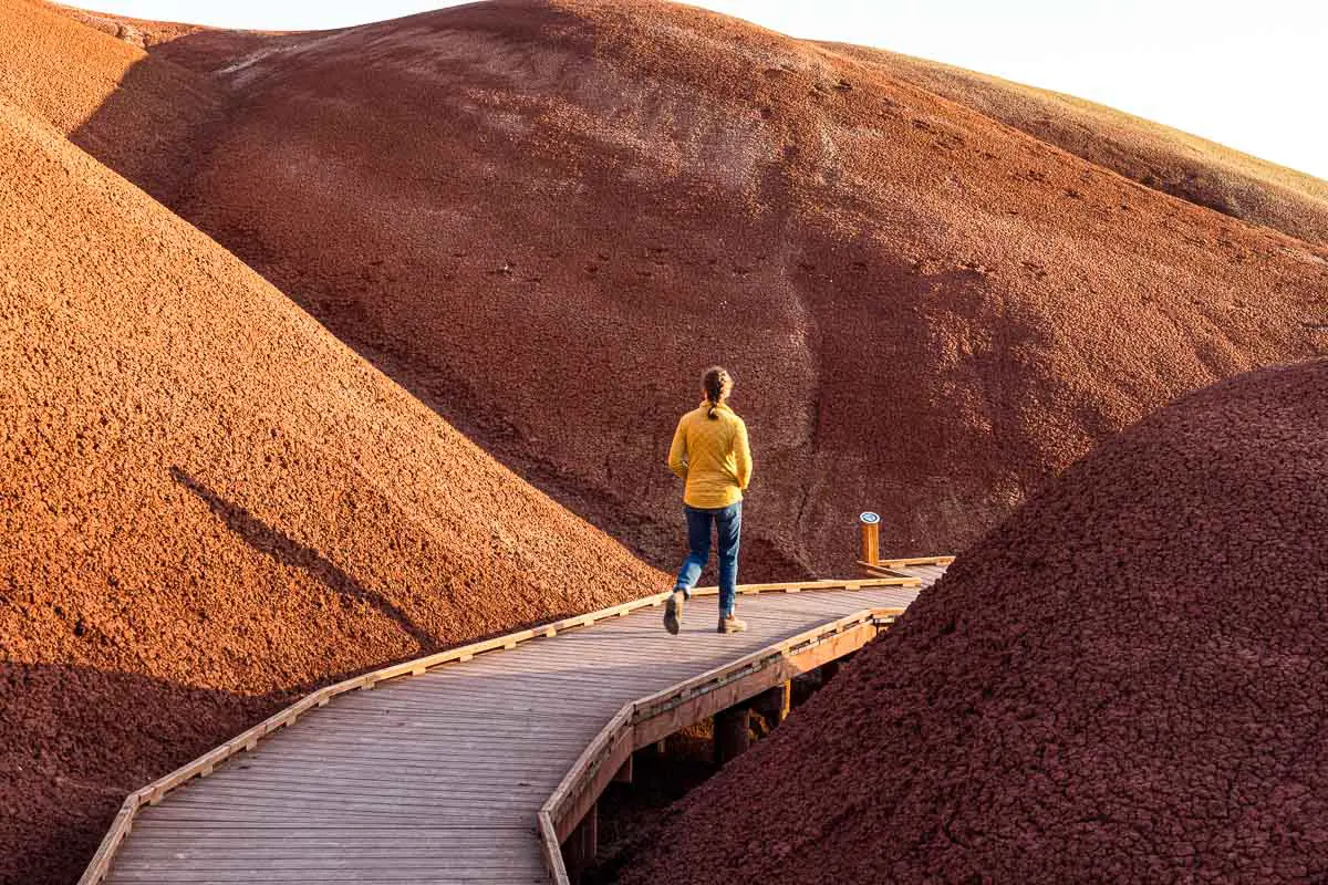 Megan walks on a boardwalk that is set between two red sand hills.