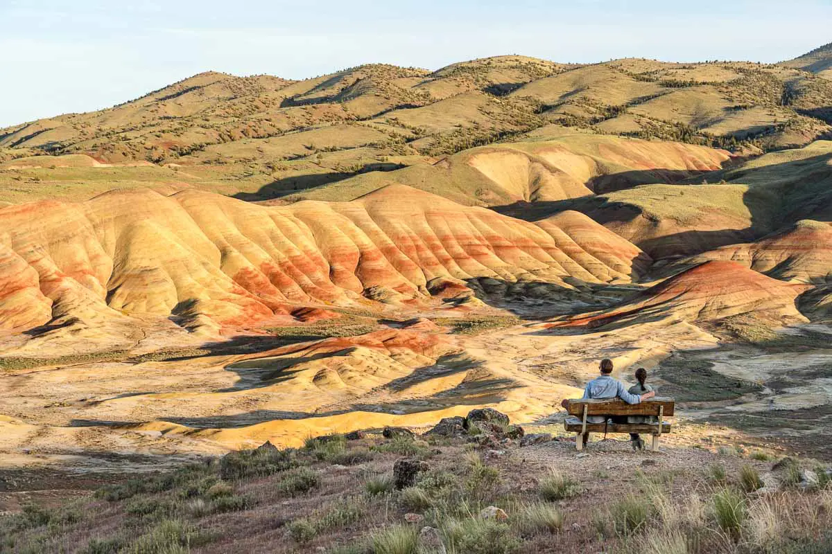 Megan and Michael sit at a bench on a overlook, looking out at the painted hills.