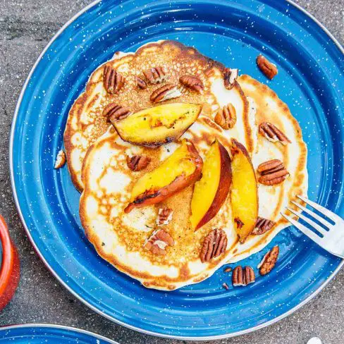 Three pancakes topped with peaches on a blue plate