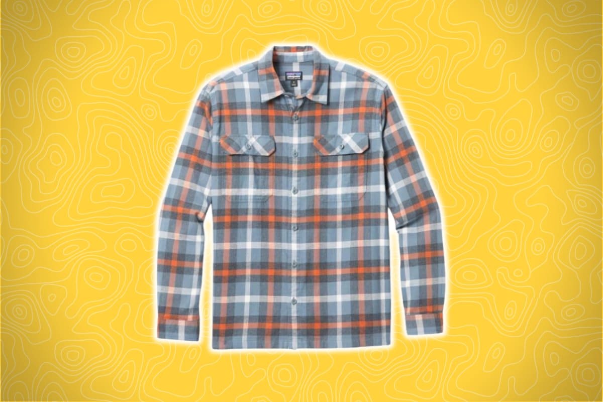A blue, orange, and white plaid flannel shirt with long sleeves and two buttoned chest pockets is displayed against a bright yellow background with a subtle abstract pattern.