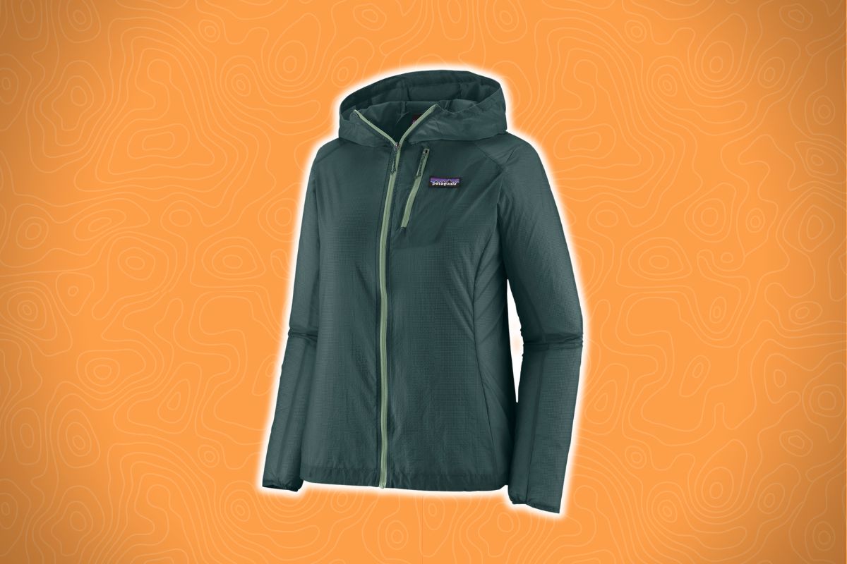 A green hooded jacket with a chest pocket and front zipper lies on an orange background with a subtle contour line pattern.