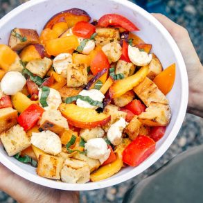 A while bowl of panzanella with torn bread, sliced peaches, tomatoes and cheese