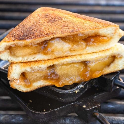 Two slices of golden-brown toasted bread with baked apple filling are stacked on a metal grill, edges crisp and caramelized.