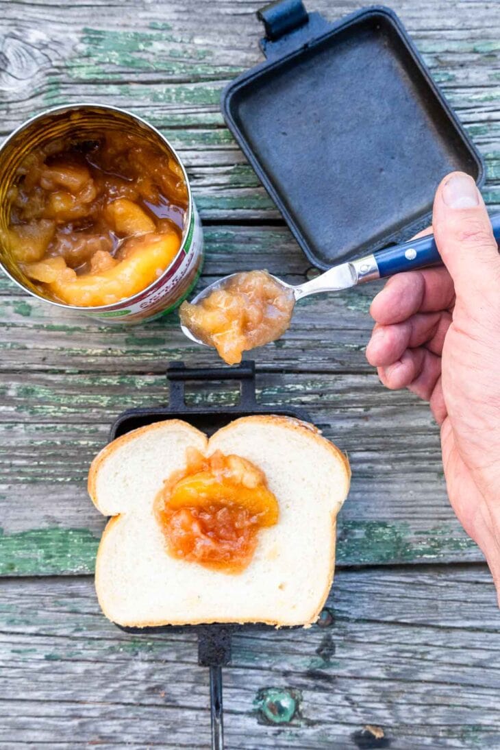Sweet canned peaches in a jar with a spoon, outdoor rustic setting, perfect for off-grid camping meals.