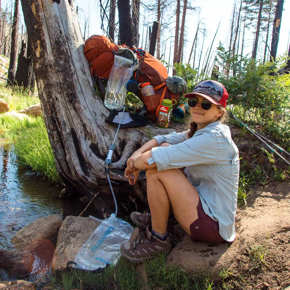 Megan sitting next to the Platypus GravityWorks water filter, which is rigged up on a tree next to a stream