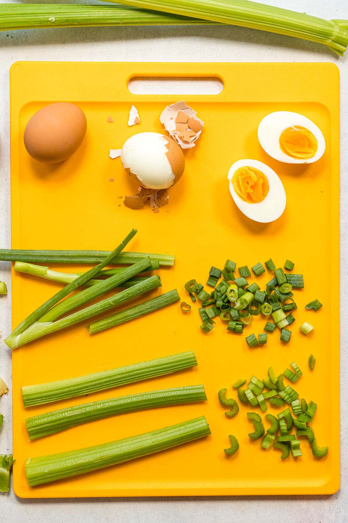 Chopped hard boiled eggs and vegetables on a yellow cutting board