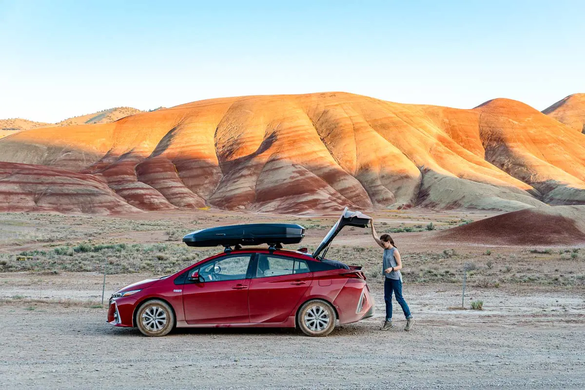 Megan is opening the trunk of a red car. The painted hills can be seen in the background.