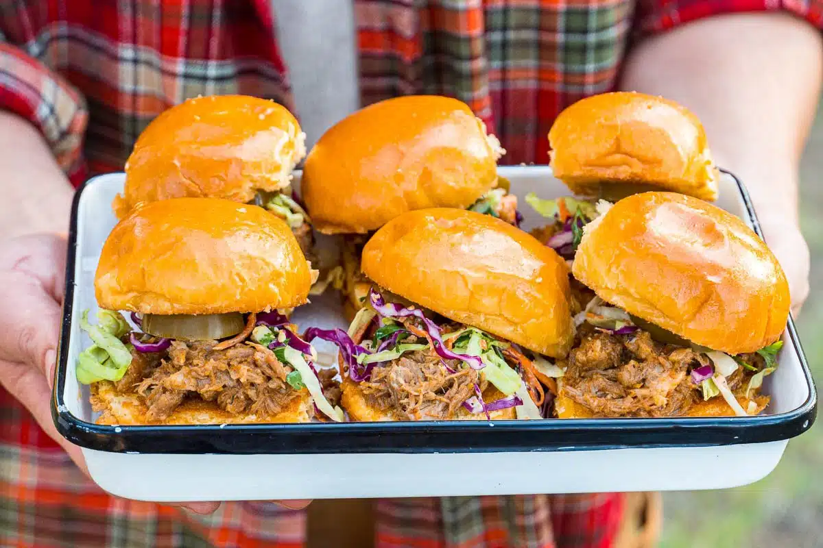 Six pulled pork sliders on a white serving dish.