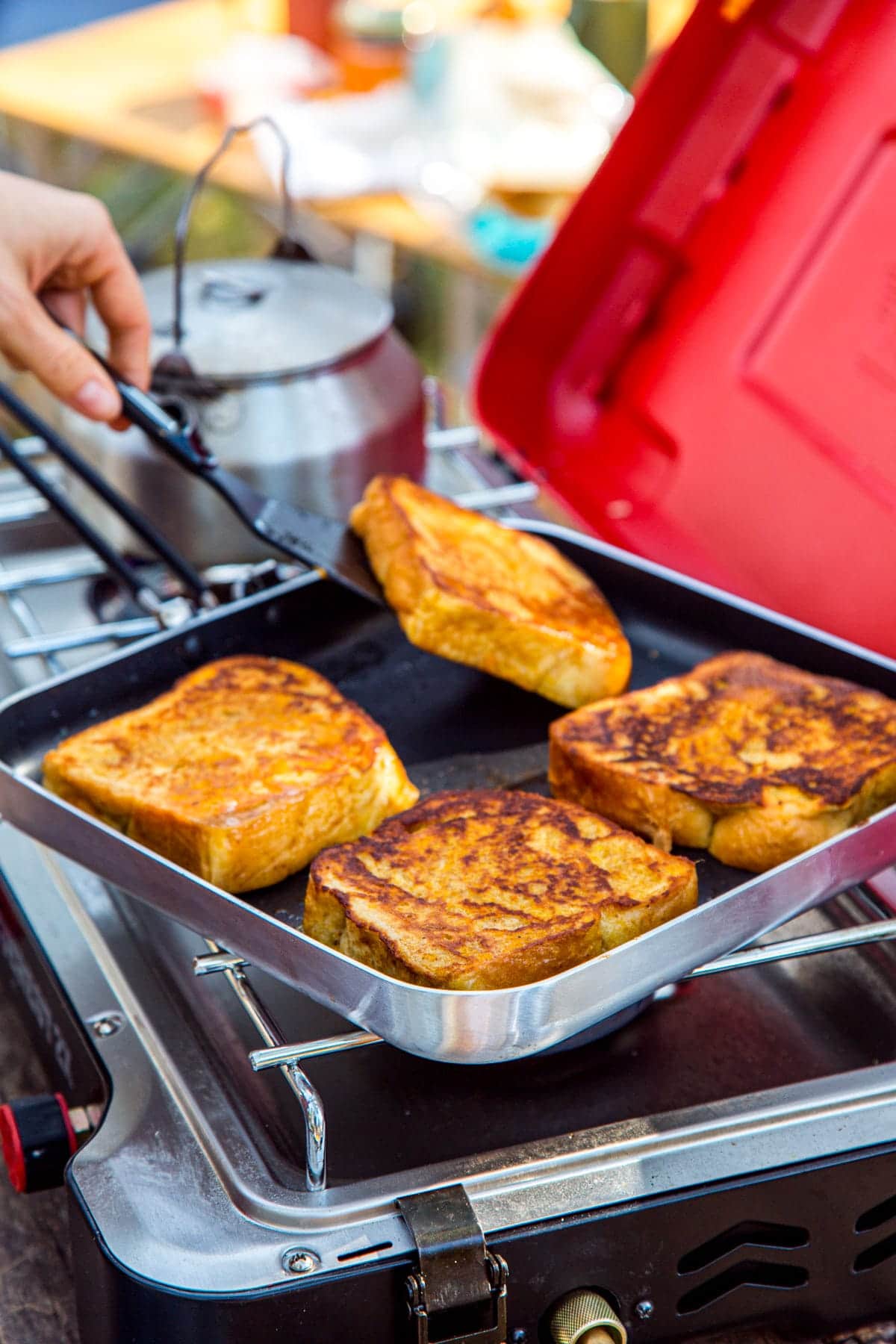 Four slices of french toast in a square skillet on a camp stove