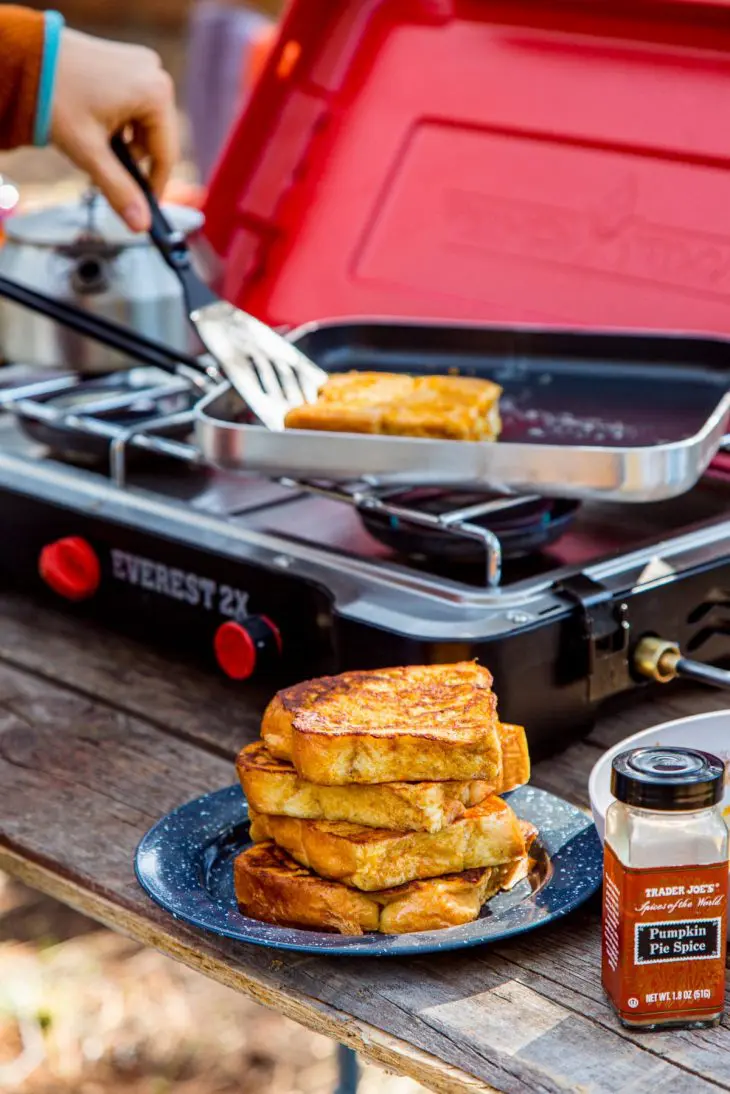A stack of french toast on a plate next to a camp stove