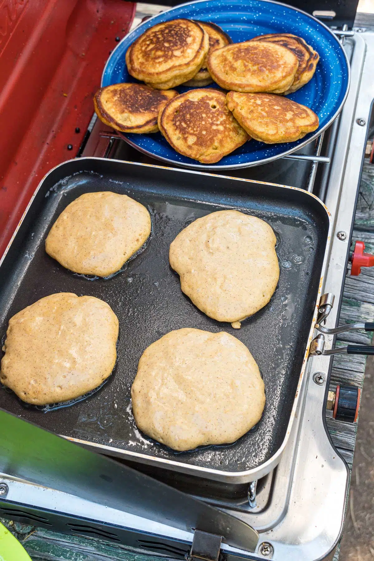 Four pancakes cooking on a square frying pan.