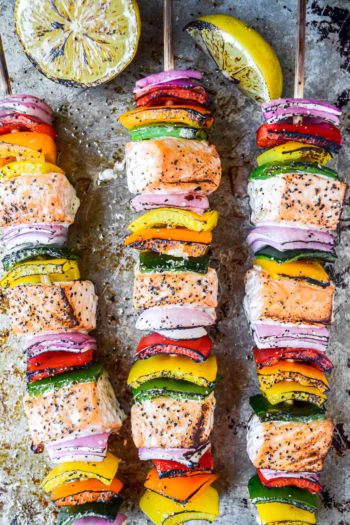 Colorful salmon and vegetable skewers ready for grilling, seasoned with herbs and spices, accompanied by lemon slices.