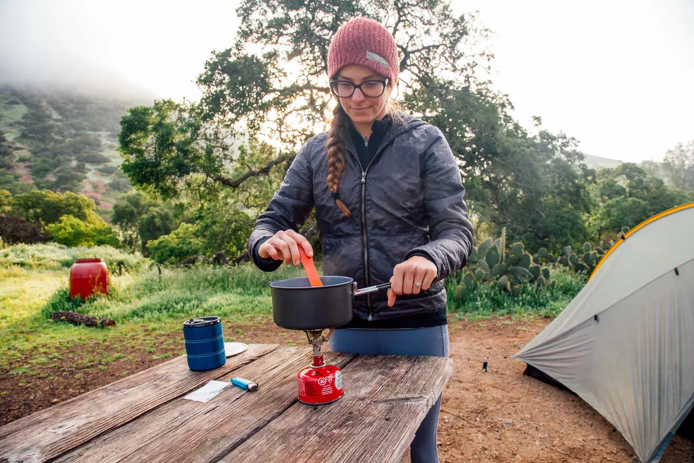 Woman cooking over a backpacking stove with a tent in the background.