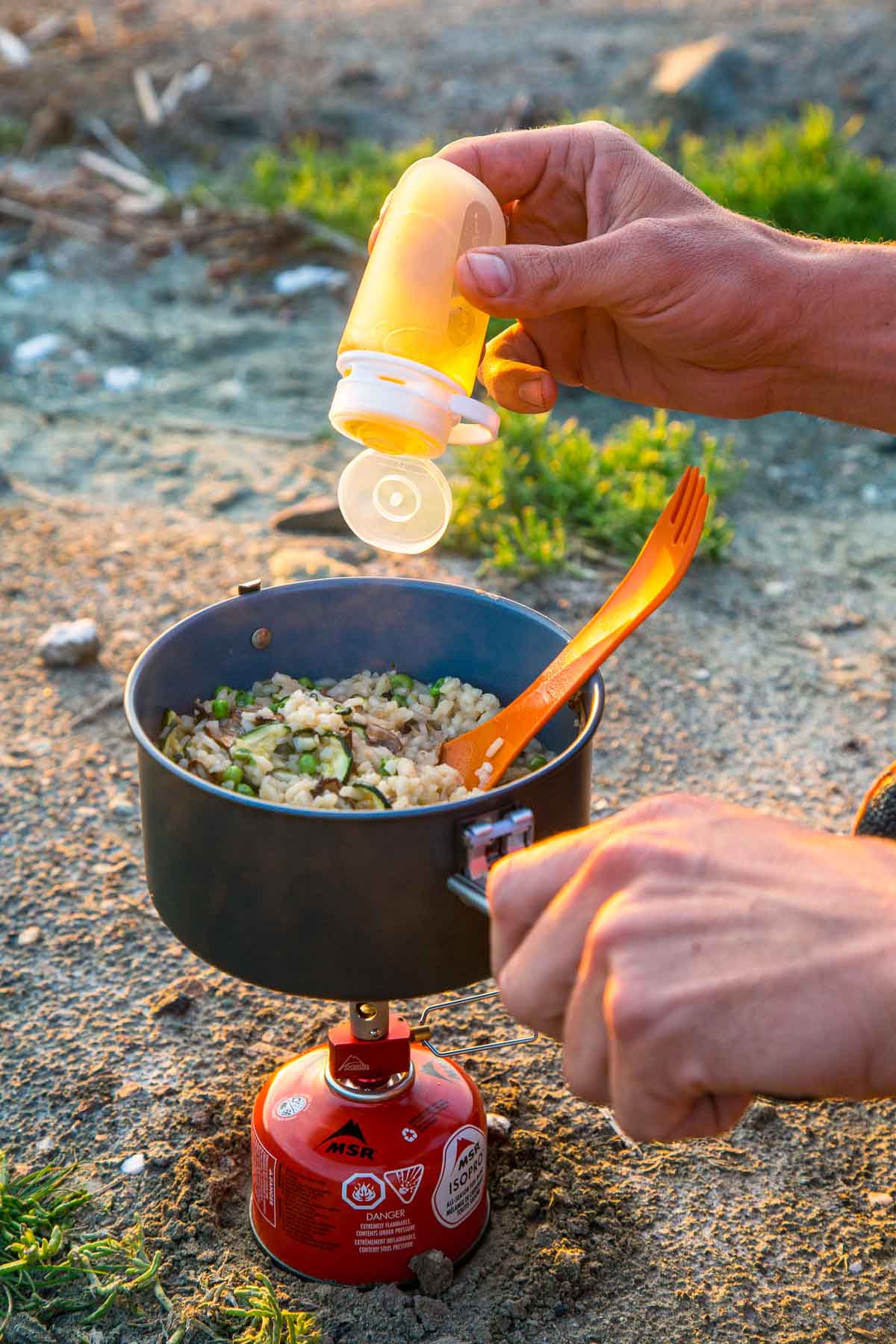 Michael adding olive oil from a squeeze bottle into a pot on a backpacking stove.